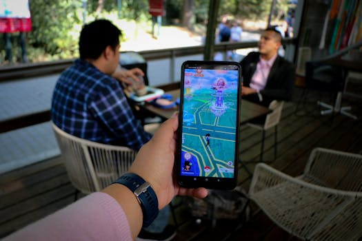 Person playing mobile game in a cafe with social interaction shown in the background.