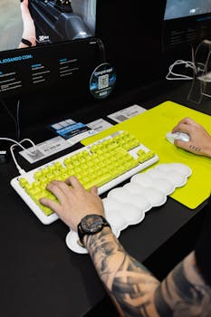 Tattooed gamer using a yellow-key mechanical keyboard and mouse at a computer trade show.
