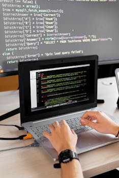Person coding at a desk with laptop and external monitor showing programming code.