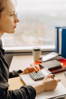 Side view of a woman using a calculator at a desk in a modern office.