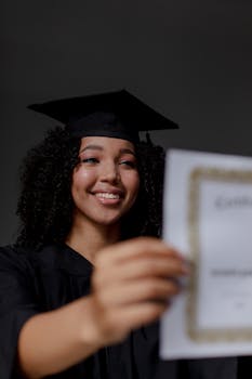 Smiling graduate woman in cap and gown holding her diploma indoors.