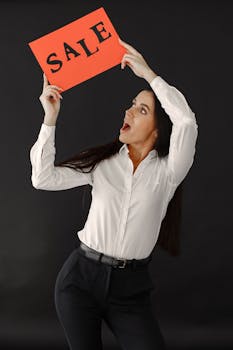 Studio shot of a woman holding a sale sign against a black background.