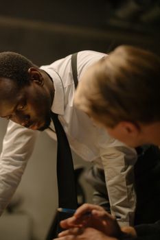 Two detectives in suits collaborating intensely over an investigation in an office setting.
